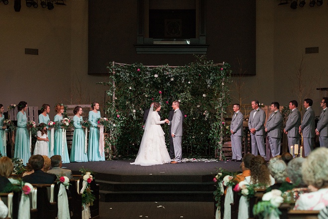 We're loving the gorgeous greenery and floral backdrop behind this gorgeous wedding ceremony!